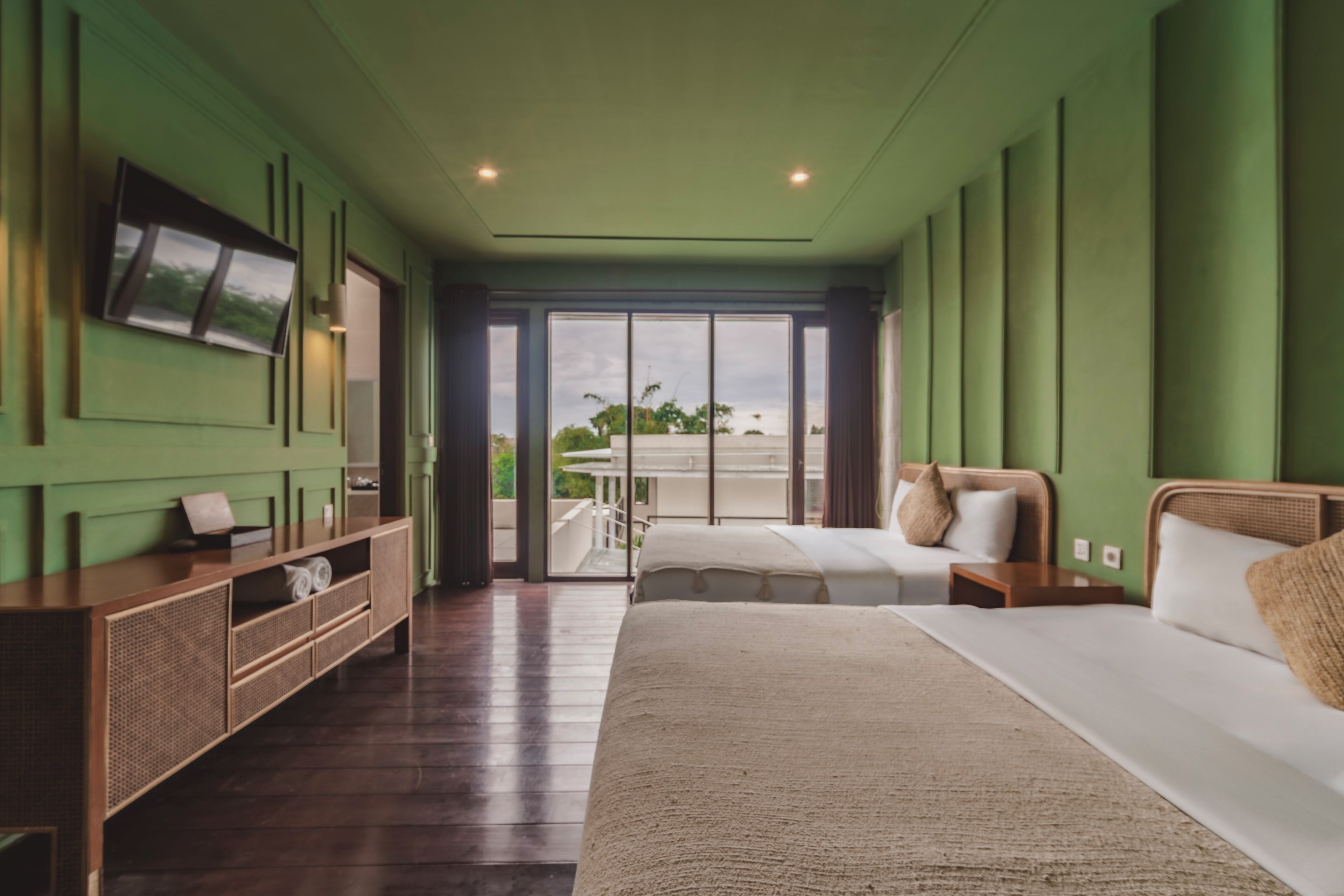 A hotel room with a large bed, a TV mounted on the wall, and a balcony with a view of the city.