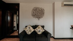 Un salon moderne avec un canapé foncé, deux coussins décoratifs, une œuvre d’art accrochée au mur et un plancher en bois.