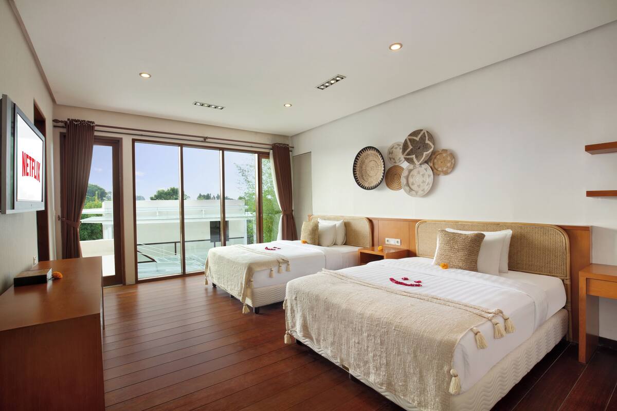 Habitación de hotel con dos camas, televisor, escritorio y balcón con vistas.