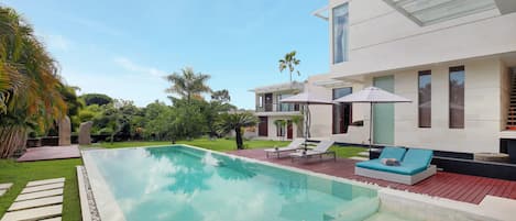 Un área de piscina moderna con una piscina cristalina, sillas de descanso y un jacuzzi.