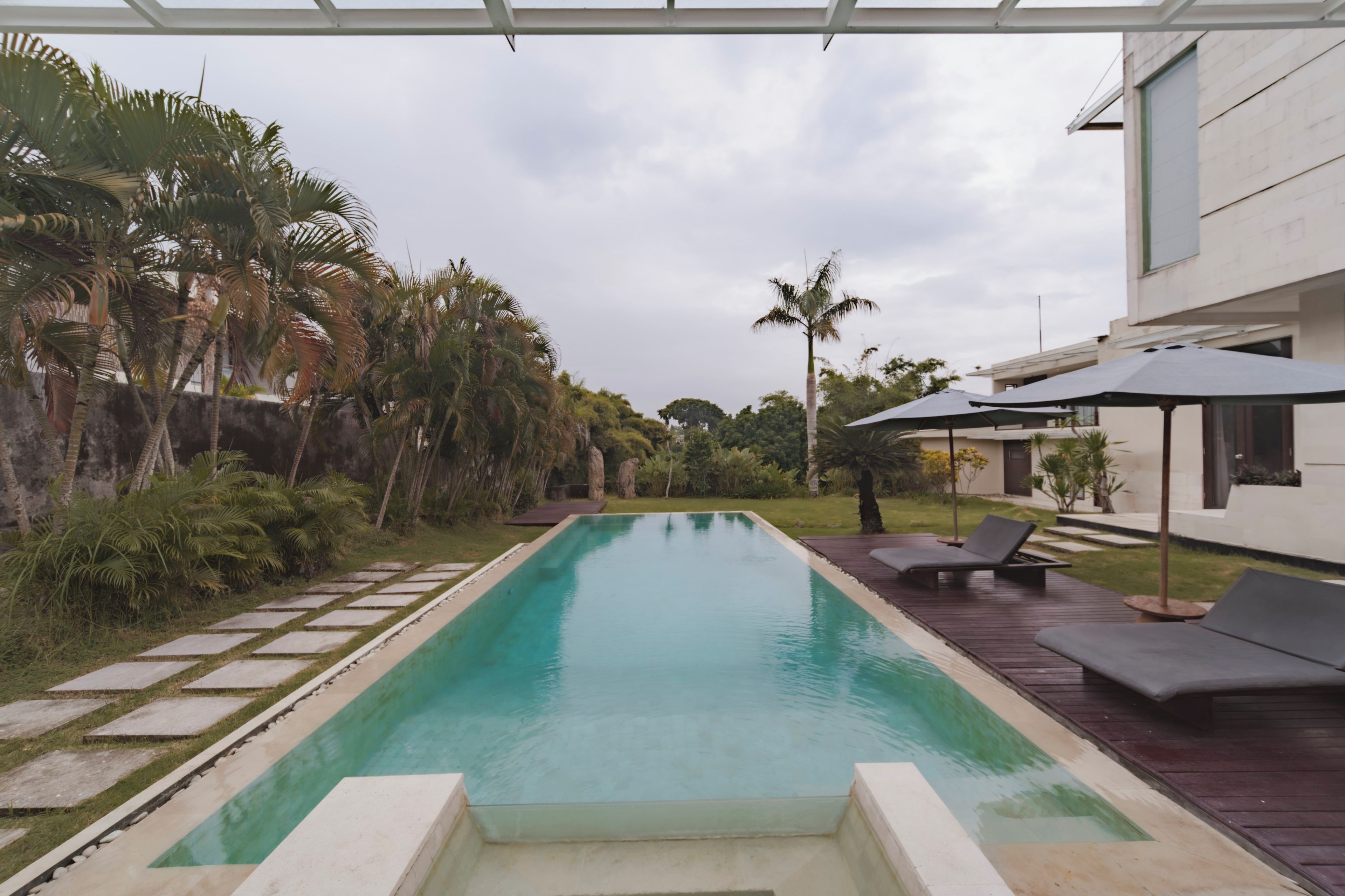 A rectangular swimming pool with a clear blue water surface, surrounded by a wooden deck and lounge chairs.