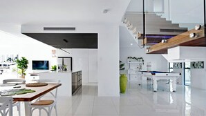 Eine moderne Küche mit weißen Schränken, ein Essbereich mit einem Holztisch und weißen Stühlen sowie ein Billardtisch im Hintergrund.