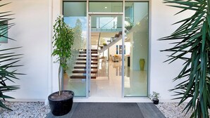 Ein moderner Eingangsbereich mit Glastür, einer Treppe zu einer oberen Ebene und einem Blumentopf am Boden.