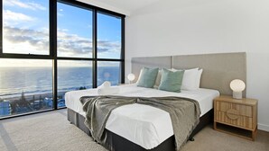 A modern bedroom with a large bed, a view of the ocean, and a wooden nightstand.