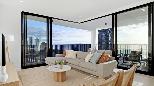 A modern living room with a sofa, coffee table, and chairs. It features large windows with a city view.