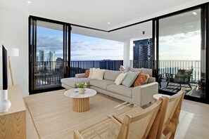 A modern living room with a sofa, coffee table, and chairs. It features large windows with a city view. - Luxury Villas Bela Casa (Ocean Views) (Gold Coast)