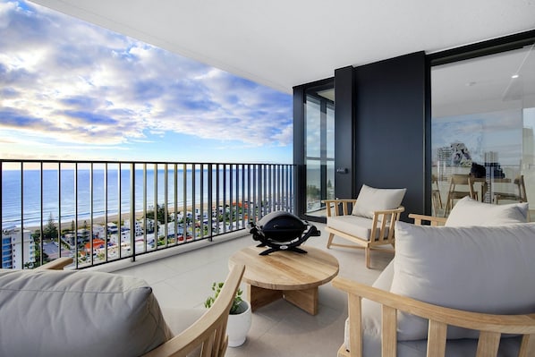 A balcony with a view of the ocean and cityscape, furnished with wooden chairs and a small table. - Luxury Villas Bela Casa (Ocean Views) (Gold Coast)
