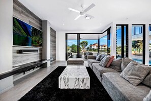 A modern living room with a flat-screen TV, a ceiling fan, a sofa, and a view of a swimming pool.