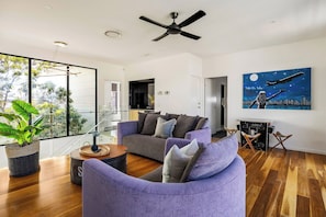 A modern living room with a grey sofa, a purple armchair, and a cityscape painting on the wall. - Luxury Villas Bluewater Oasis (Heated Pool) (Gold Coast)