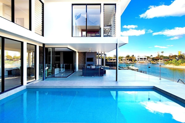 A modern house with a swimming pool, large glass doors, and a view of the water.