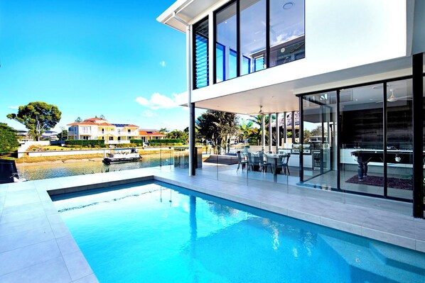 A modern house with a swimming pool, glass doors, and a view of the water.