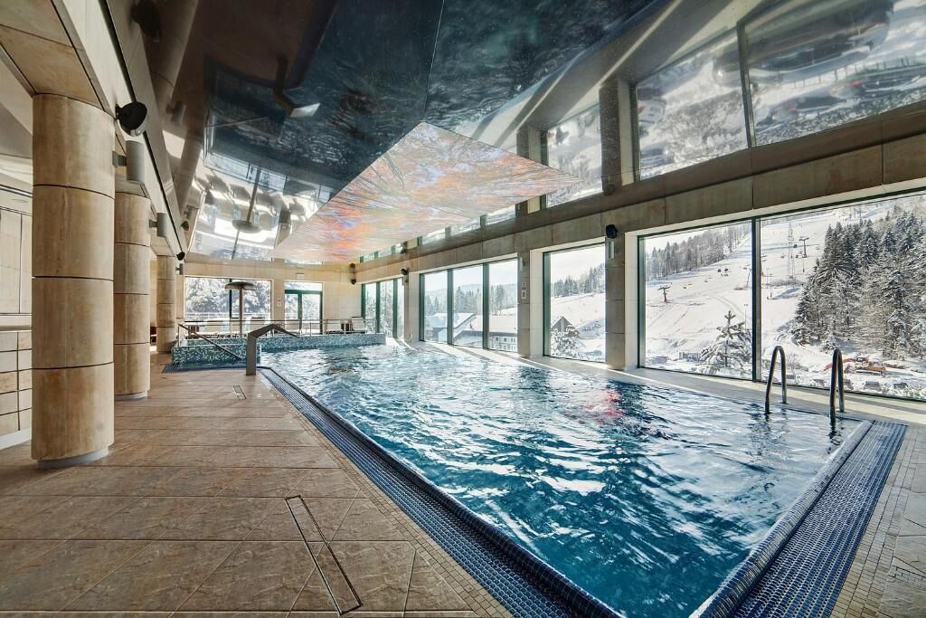 An indoor swimming pool with clear windows overlooking a snowy landscape.