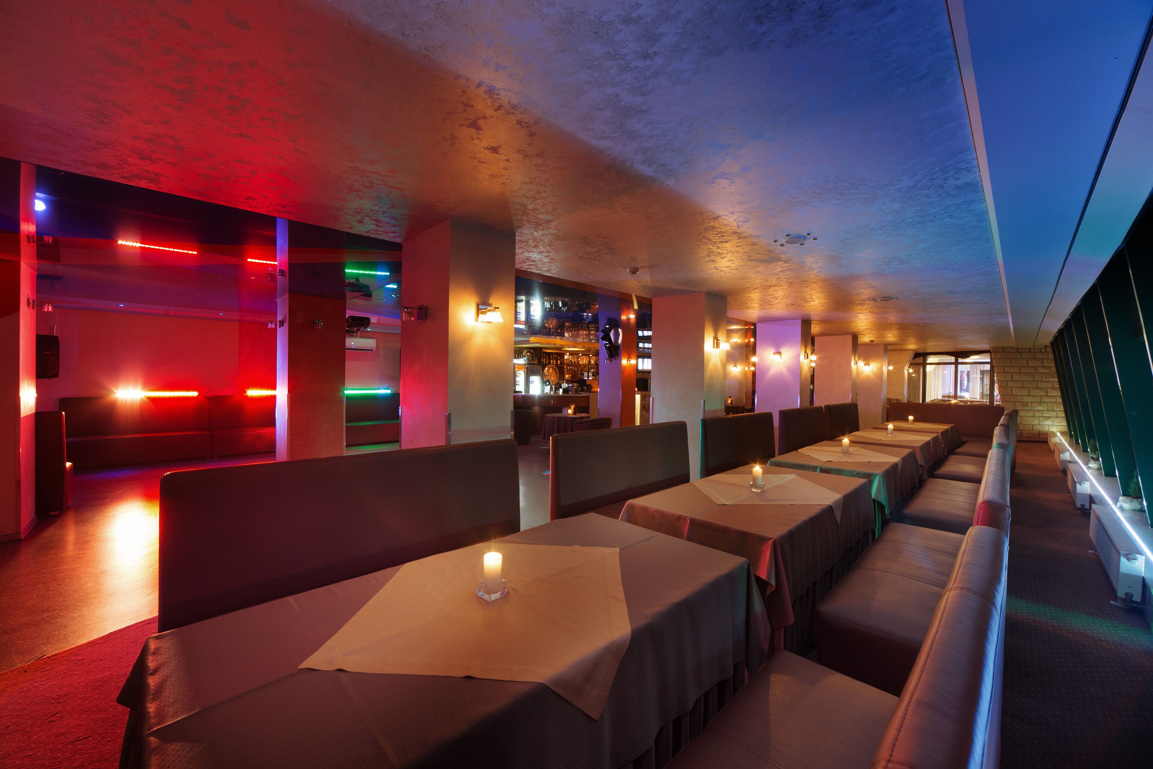 Un restaurante con cabinas y mesas, iluminación ambiental y una zona de bar al fondo.
