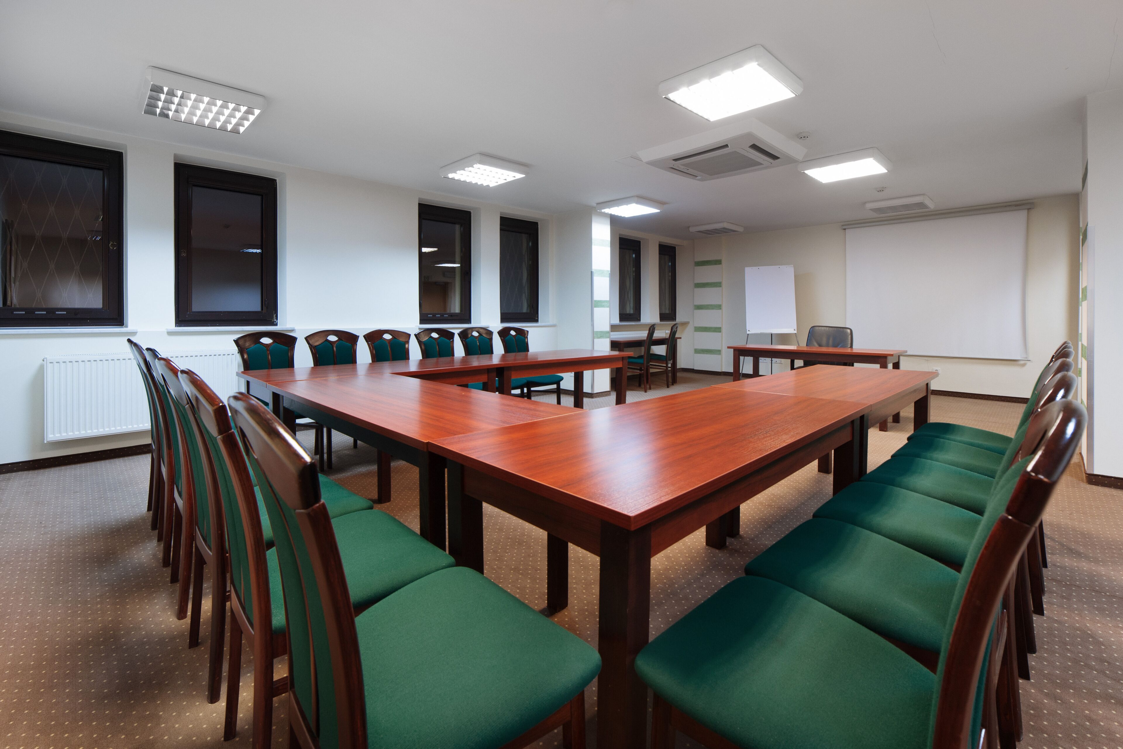 Un salón de conferencias con una larga mesa de madera, sillas tapizadas en verde y una pizarra.