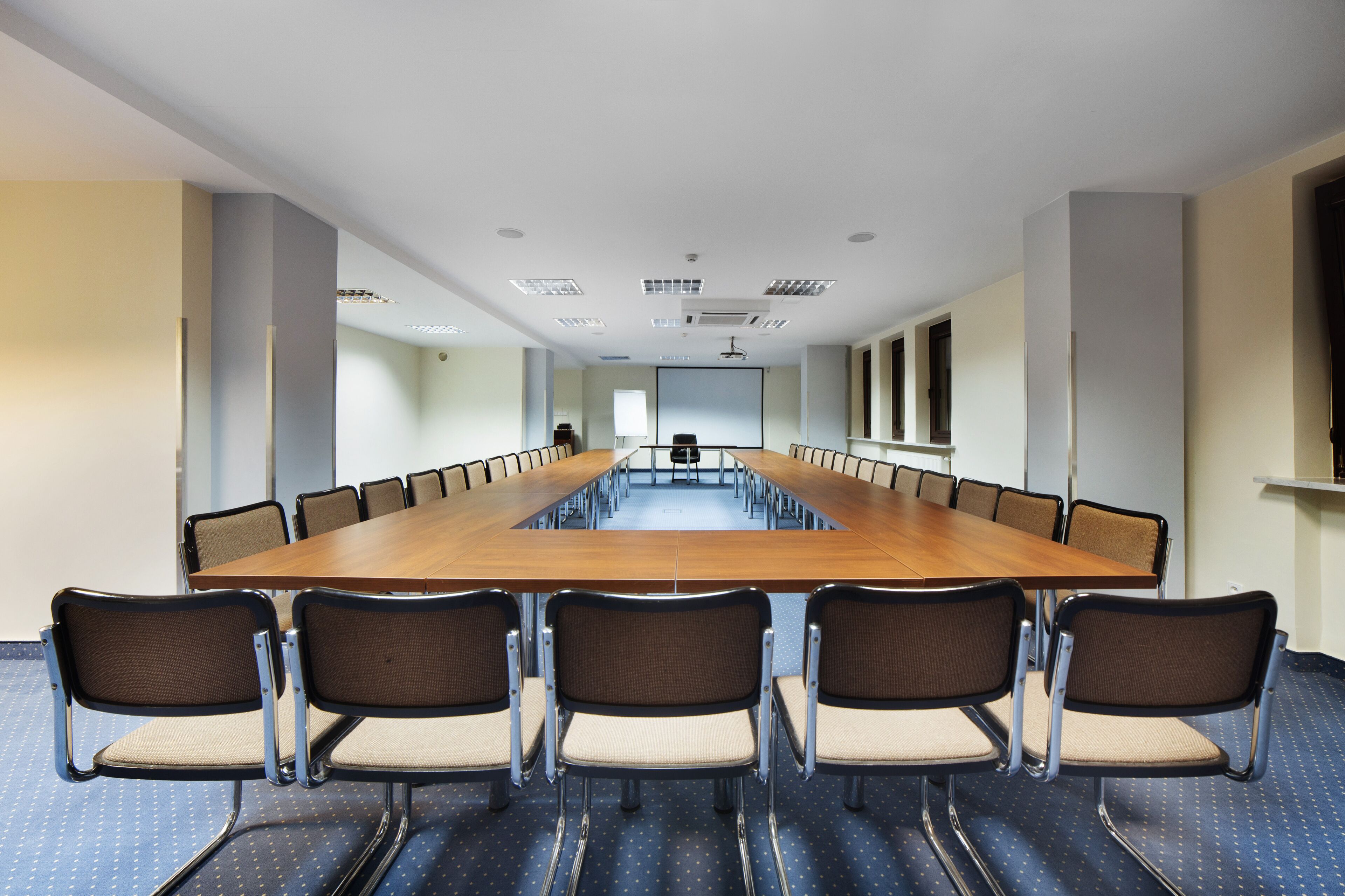 A conference room with a long table and chairs, white walls, and ceiling lights.