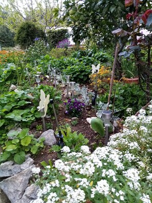 Um jardim com diversas plantas e flores, incluindo flores brancas e roxas, e várias luminárias de jardim de metal.