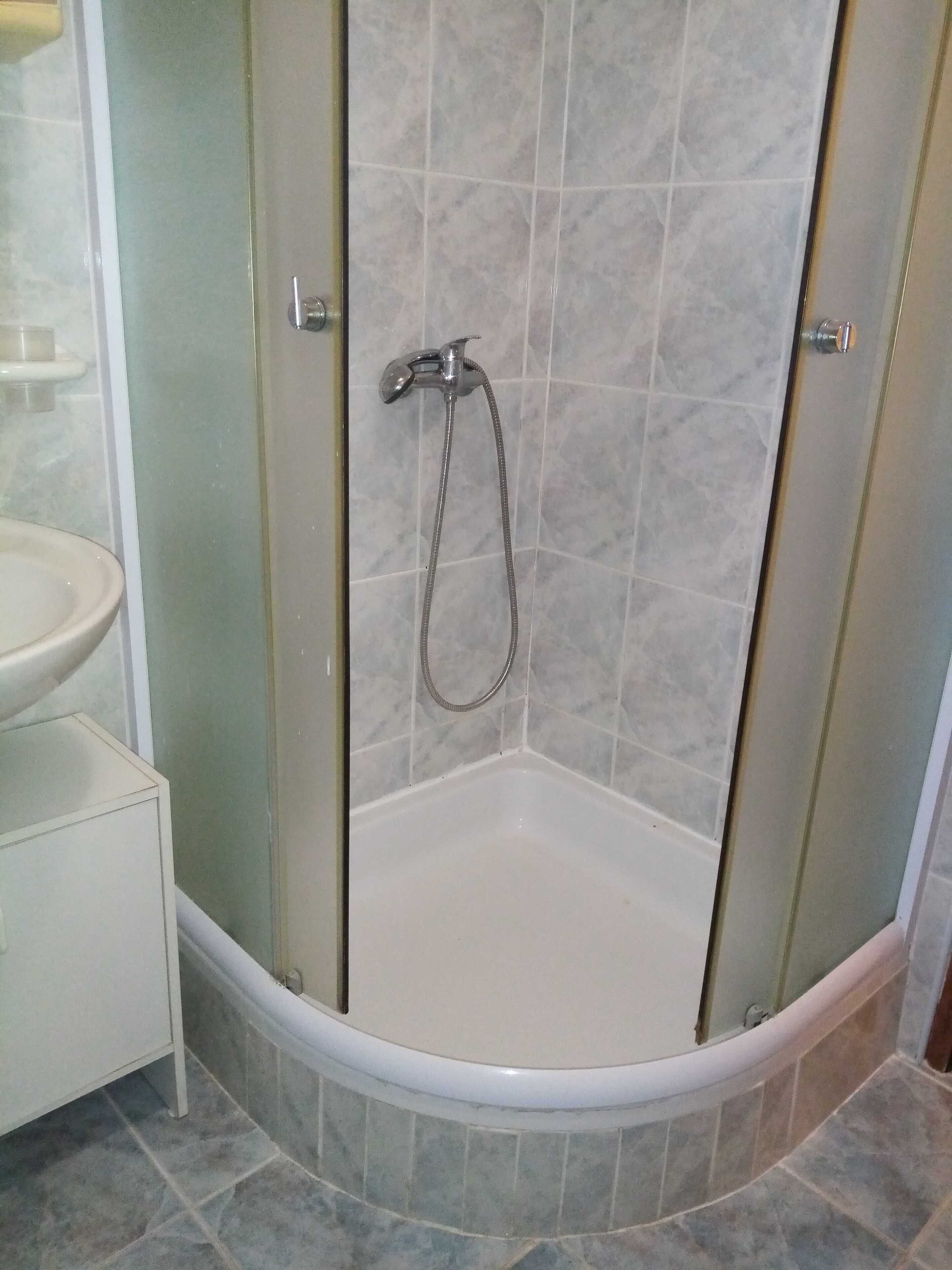 A corner shower with a glass door, a white sink, and a tiled floor.