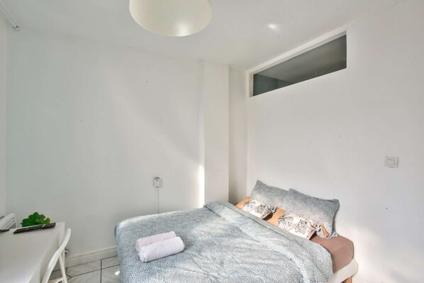 A bedroom with a bed, a desk, and a small window.