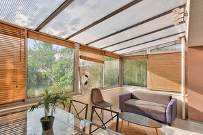 A conservatory with a glass table, chairs, a sofa, and a potted plant.