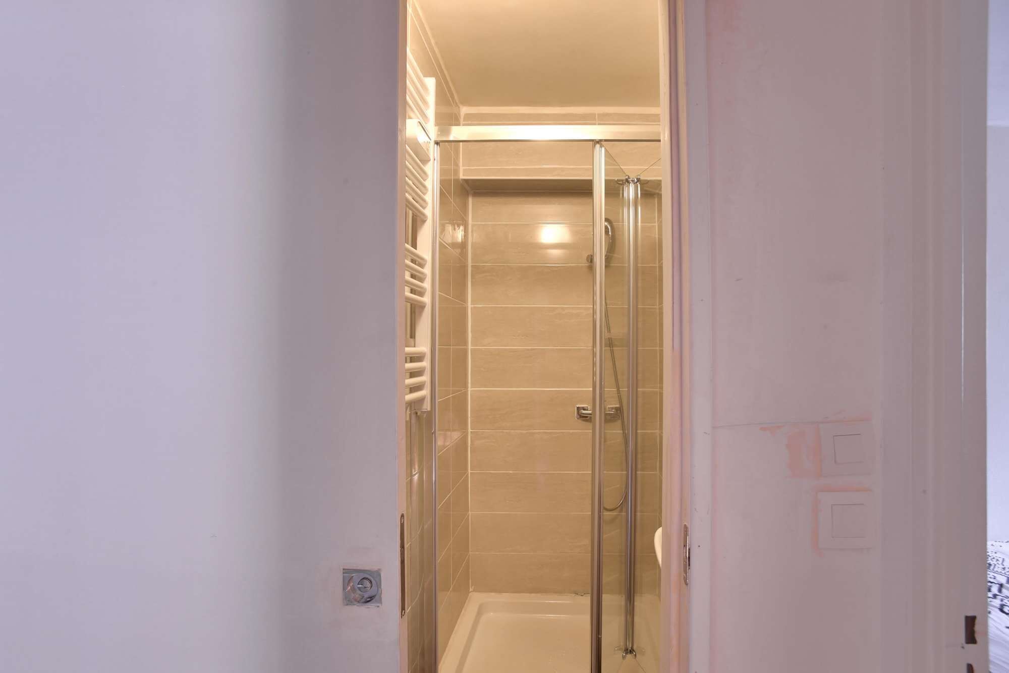 A glass-enclosed shower area with beige tiles and a visible handrail.