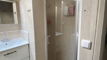 Un baño con ducha envuelta en vidrio, un lavabo con espejo y suelo de azulejos.