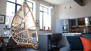 A modern kitchen with a hanging chair, a dining area, and a sofa with cushions. - Trafalgar Lane (Edinburgh)