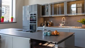 A modern kitchen with a central island, stainless steel appliances, and a window with plants. - Trafalgar Lane (Edinburgh)