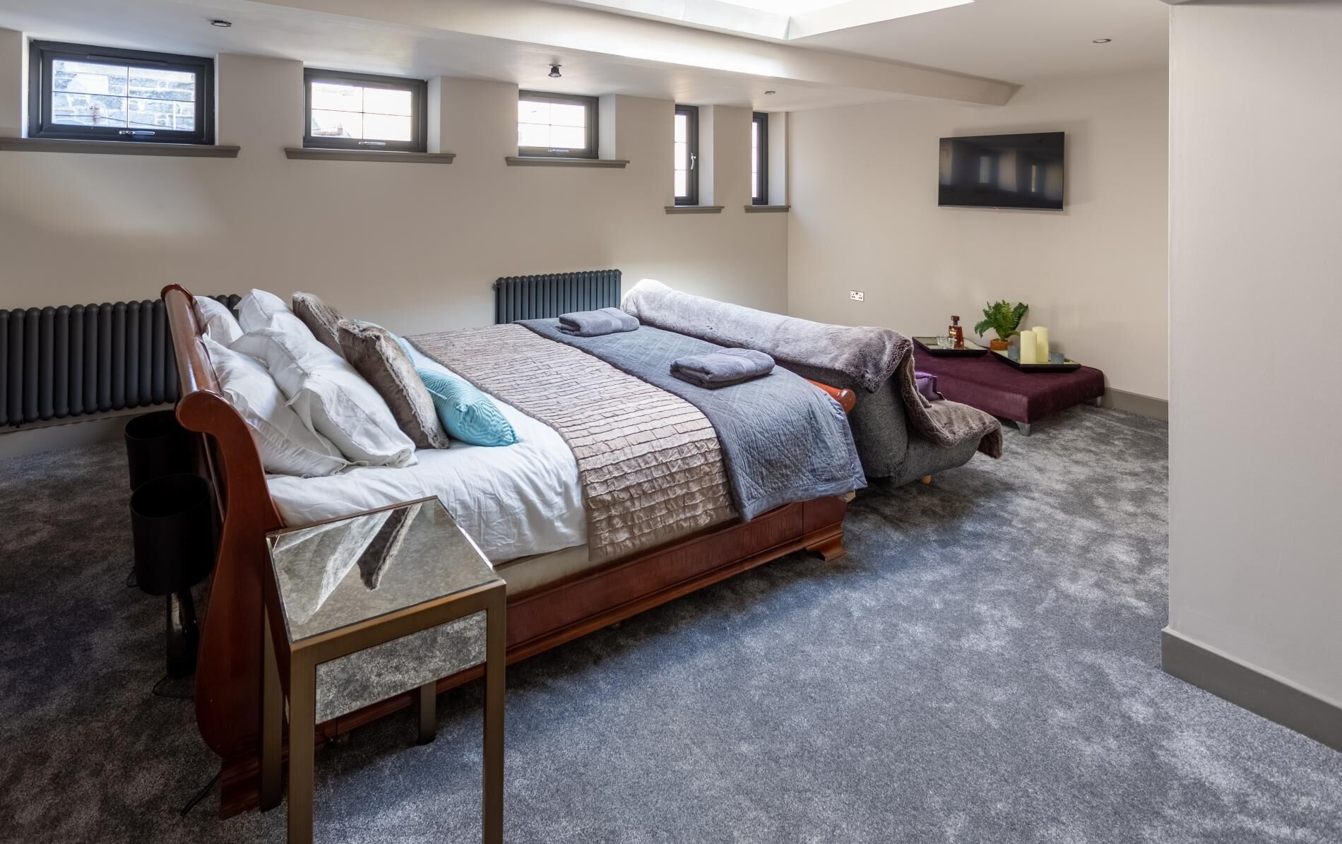A bedroom with a large bed, a radiator, a TV, and a small table with candles and a plant.