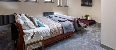 A bedroom with a large bed, a radiator, a TV, and a small table with candles and a plant.