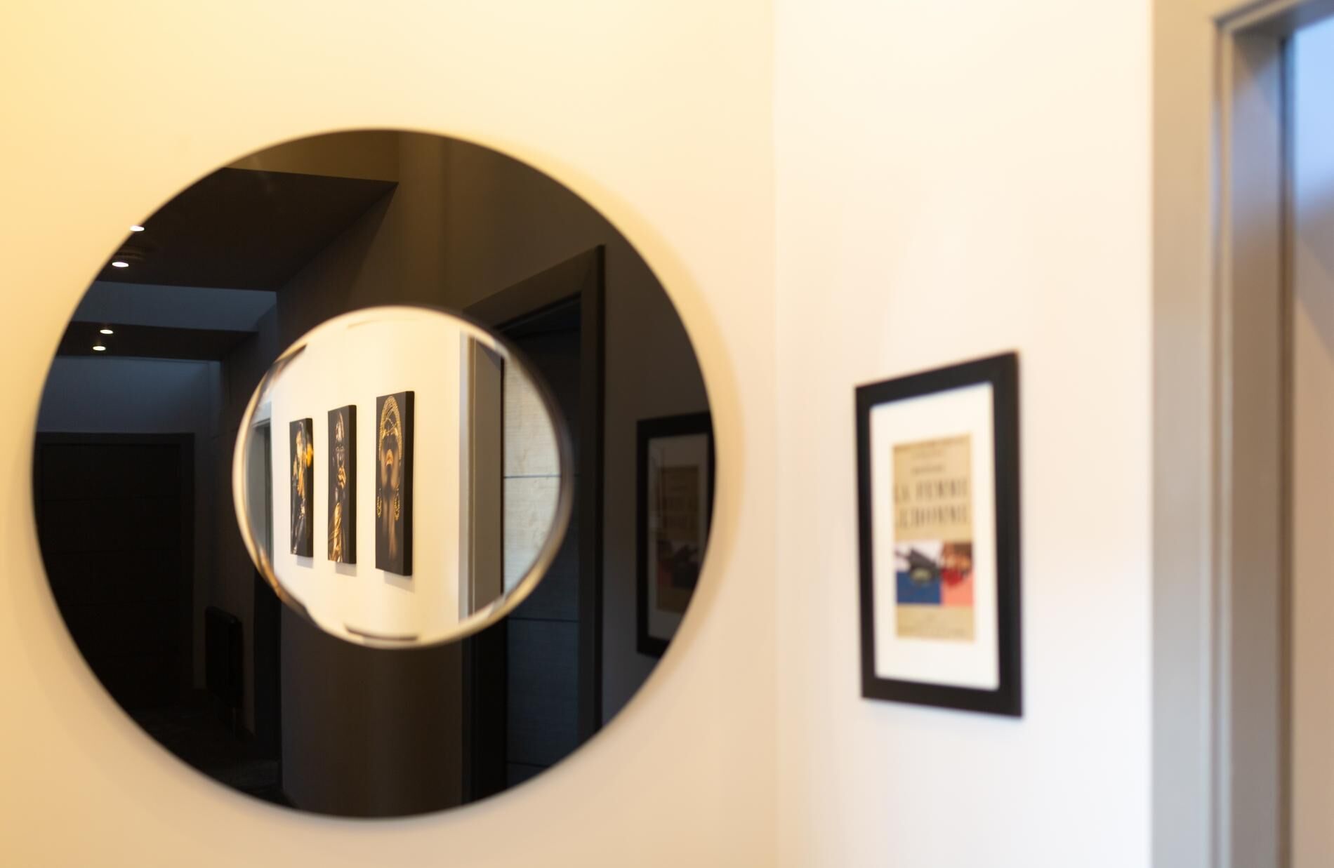 Un miroir rond fixé au mur, qui reflète une œuvre d’art et une image encadrée.