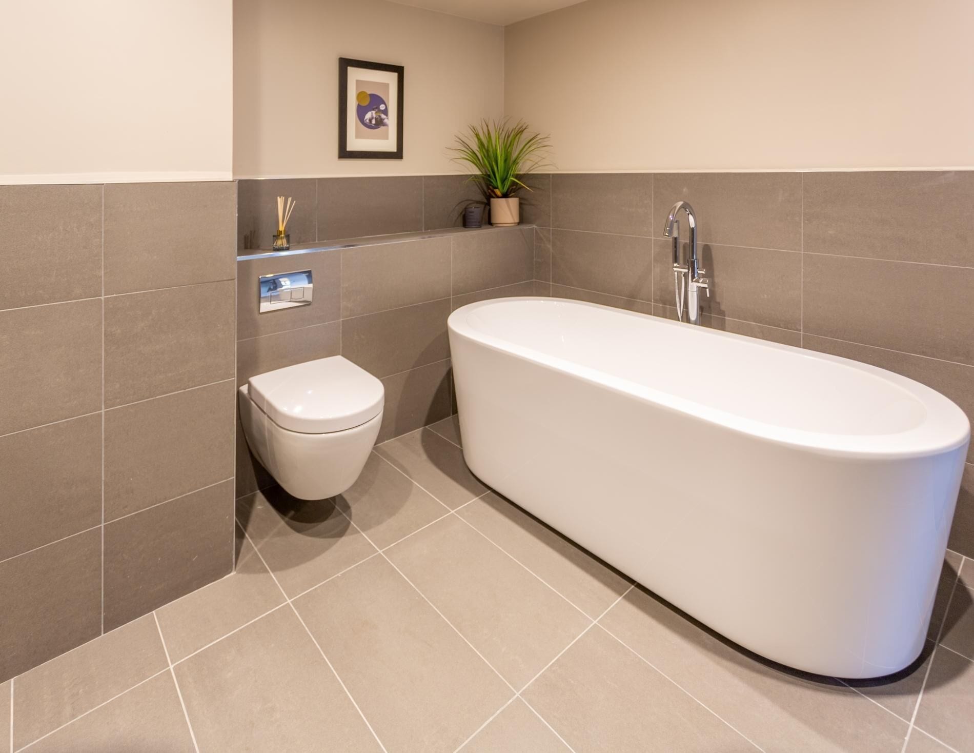 A modern bathroom with a white bathtub, a toilet, and a potted plant.