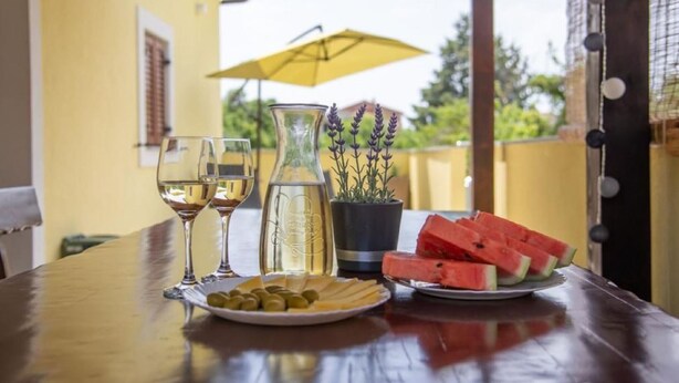 A table with a bottle of white wine, two glasses, a plate of olives, a plate of watermelon slices, and a potted lavender plant.