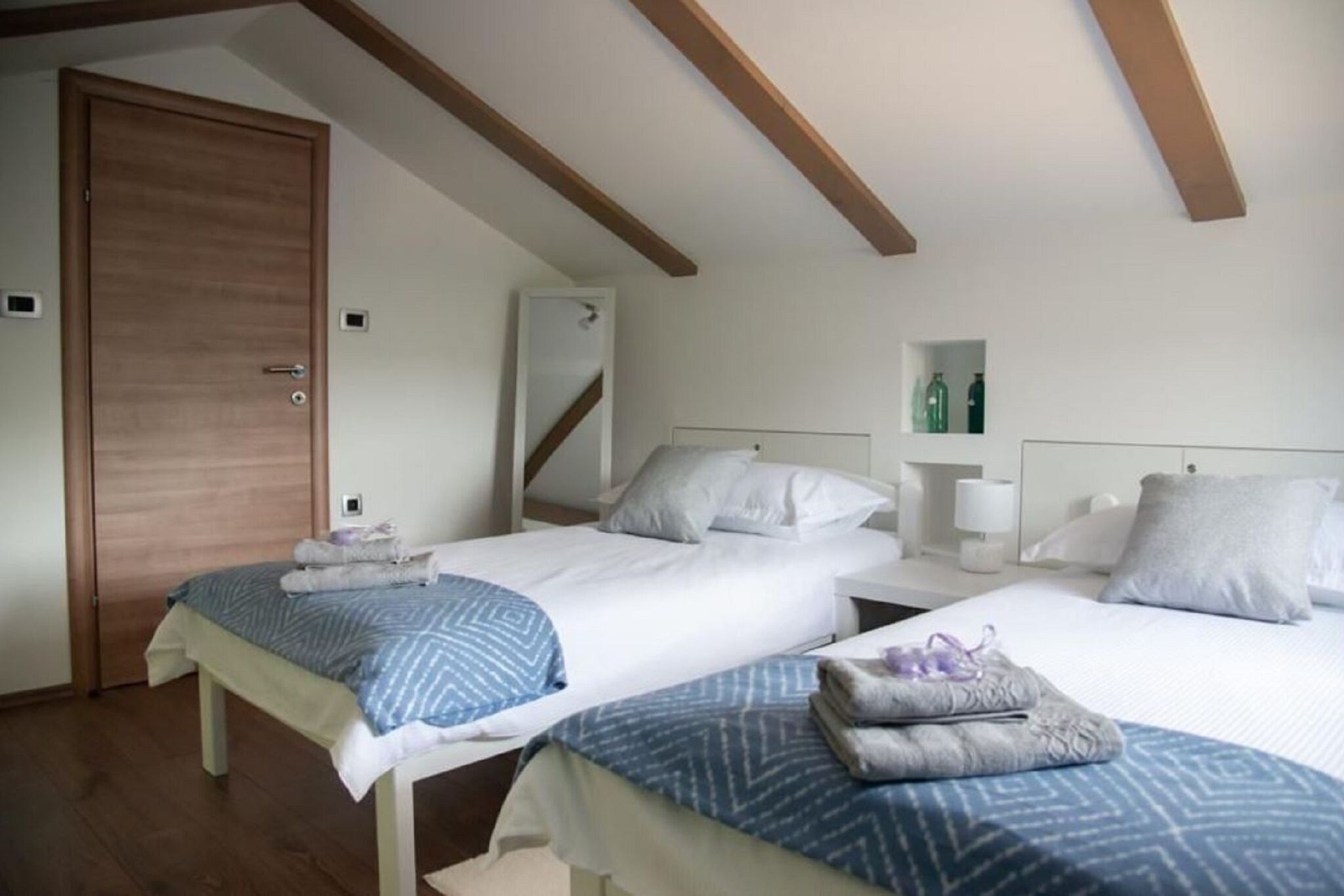 Ein Hotelzimmer mit zwei Betten, Holzbalken an der Decke, einem Kleiderschrank und einem kleinen Regal mit Flaschen.