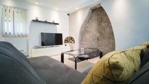 A modern living room with a flat-screen TV, a glass coffee table, and a stone fireplace.