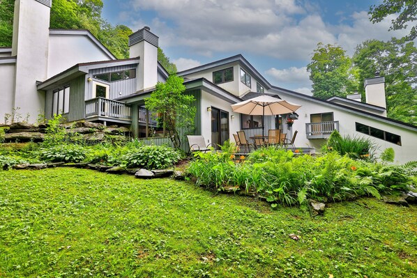 A modern house with a landscaped garden, a patio with outdoor furniture, and a large umbrella.