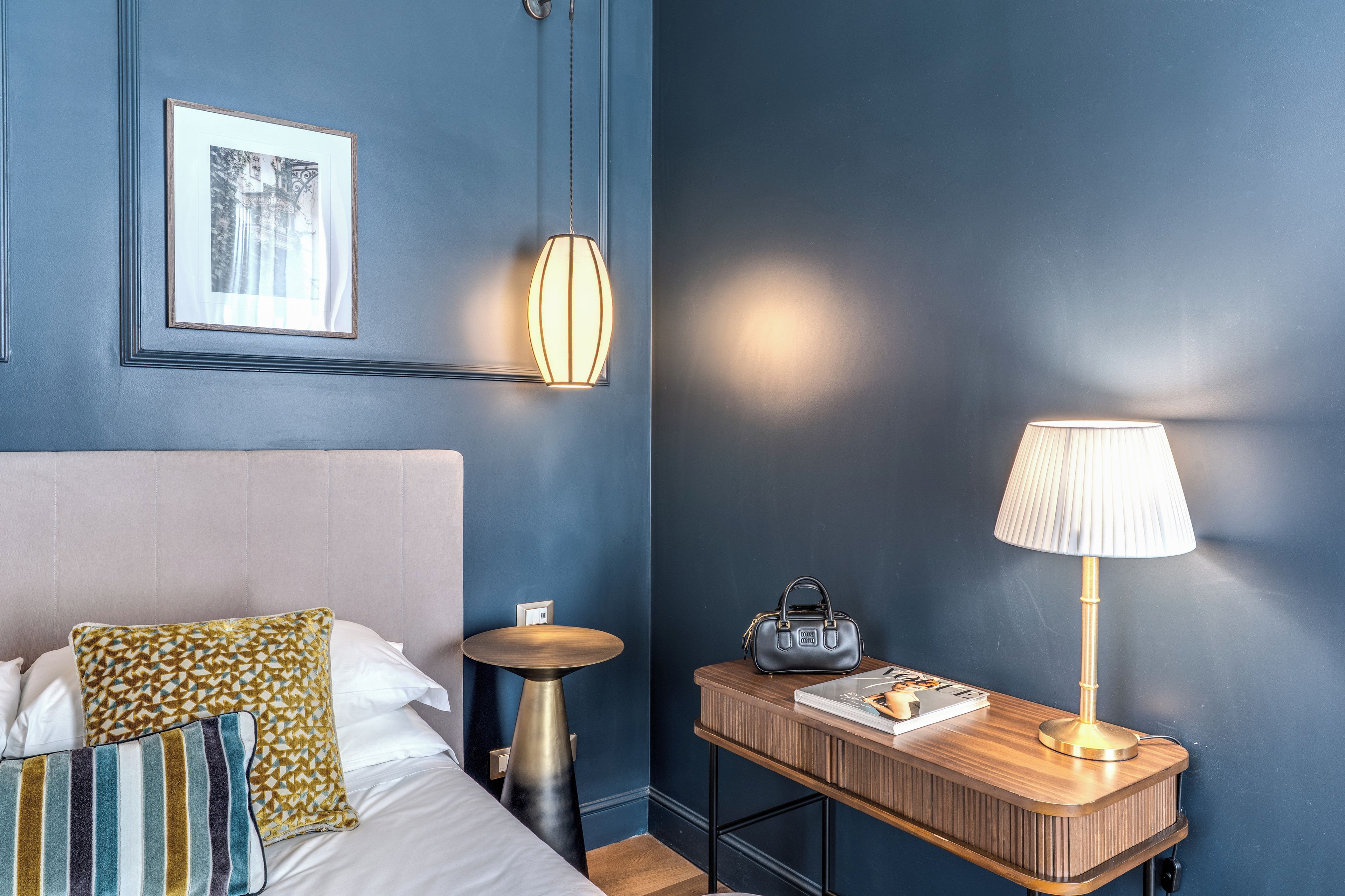 A hotel room with a bed, bedside table, lamp, and a framed picture on the wall.
