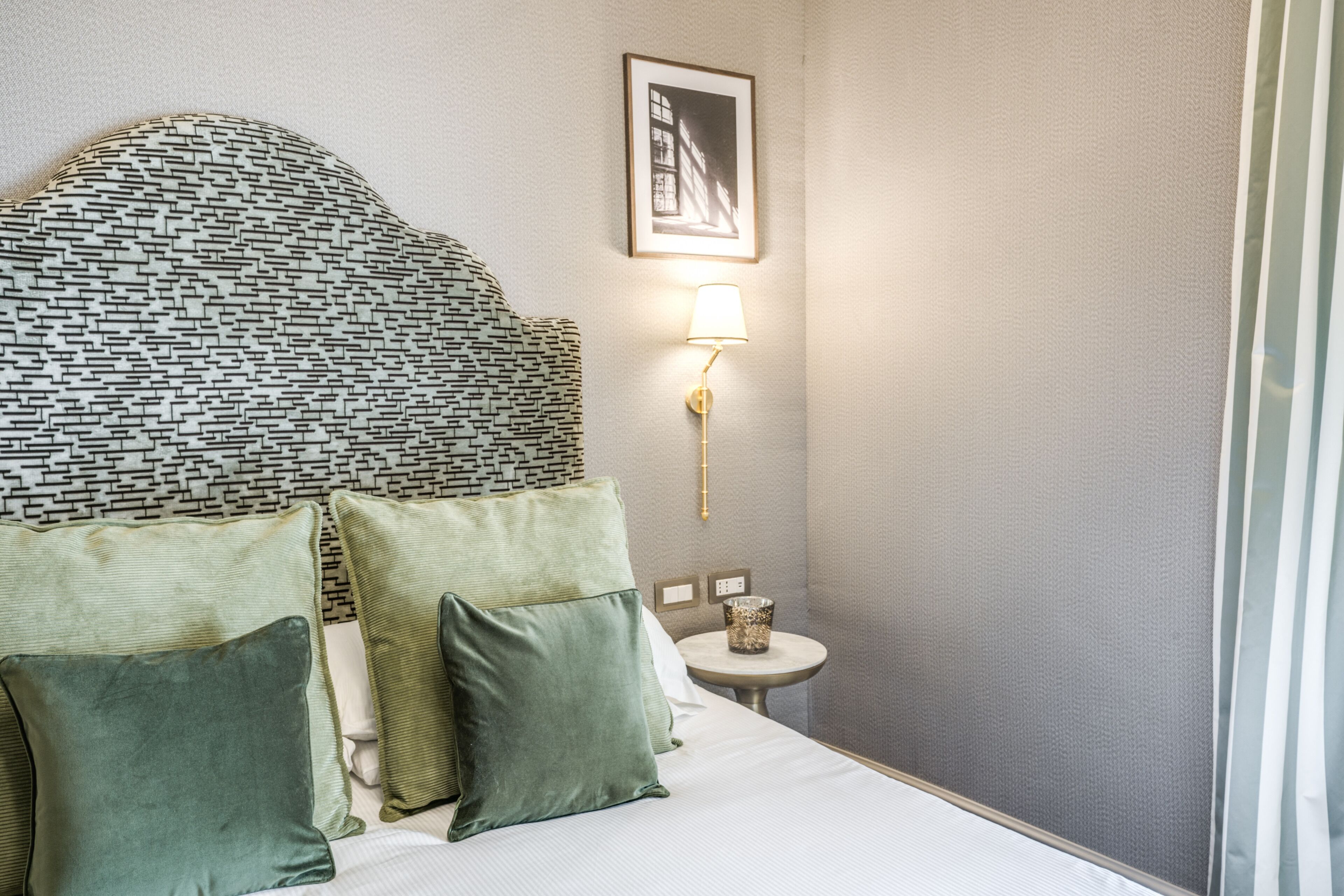 A neatly arranged hotel room with a patterned headboard, a bedside table with a lamp, and a framed picture on the wall.