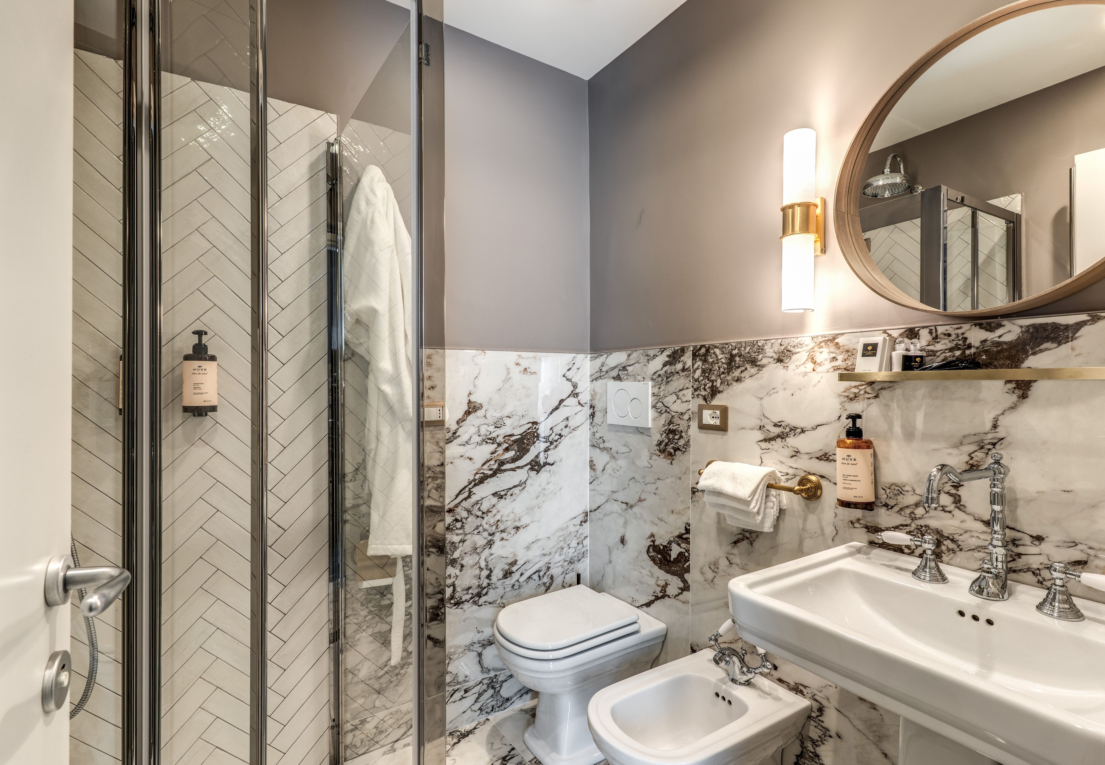 Een moderne badkamer met een douchecabine van glas, een toilet en een wastafel met een marmeren spatwand.