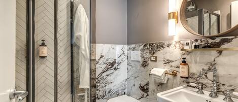 Et moderne badeværelse med brusekabine i glas, toilet og håndvask med marmorbeklædt væg.