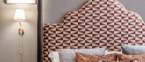 A neatly arranged hotel room with a patterned headboard, a wall-mounted lamp, and a framed picture above the bed.