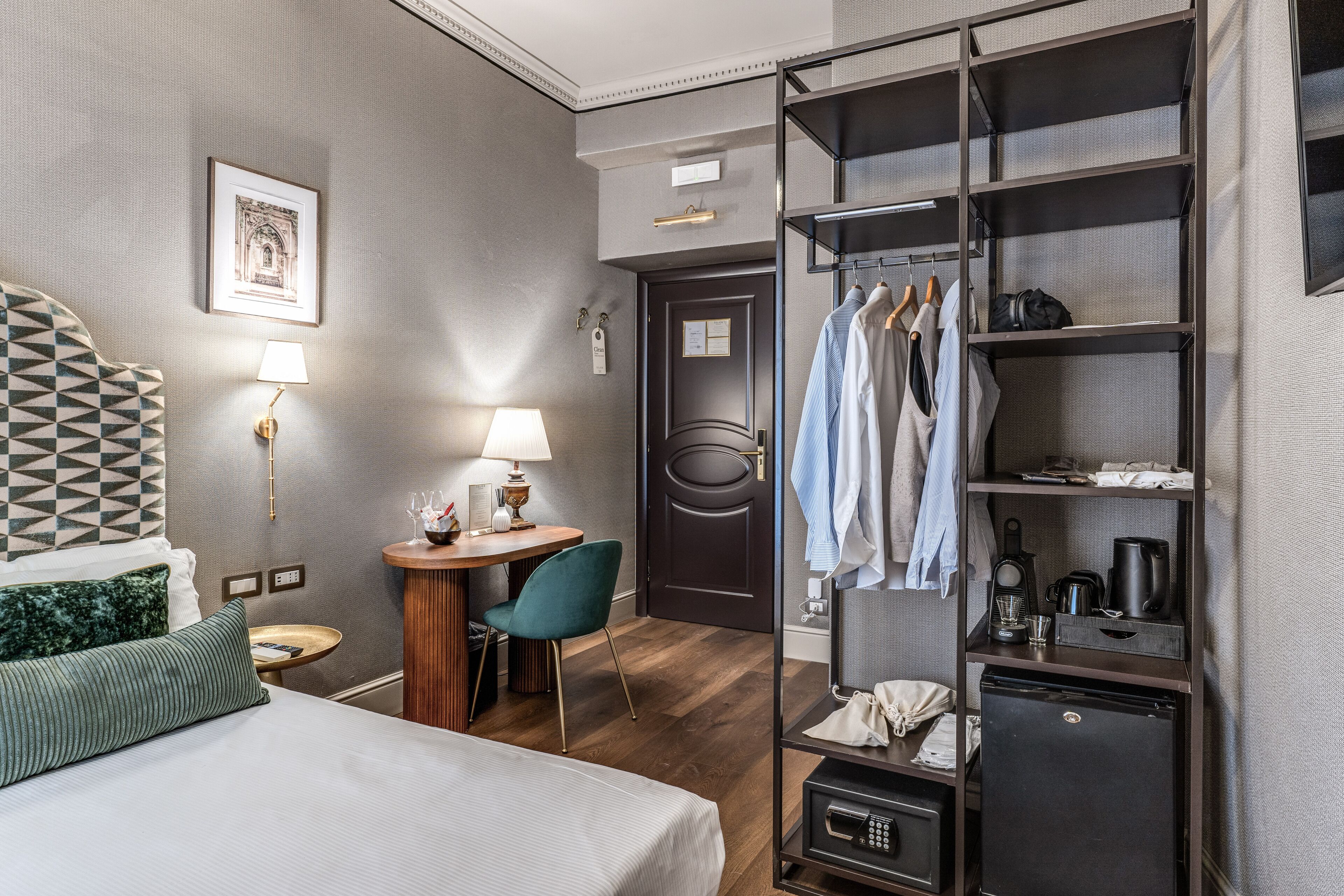 A hotel room with a bed, a desk with a lamp, a chair, a wardrobe, and a small refrigerator.