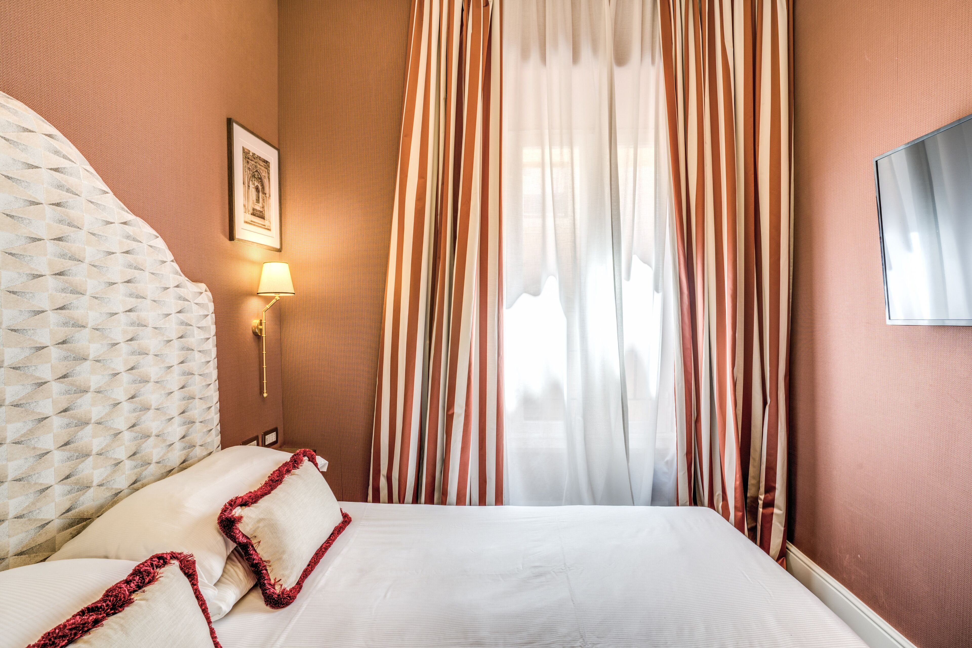 Ein Hotelzimmer mit einem großen Bett, gestreiften Vorhängen, einem gerahmten Bild an der Wand und einem an der Wand befestigten Fernseher.