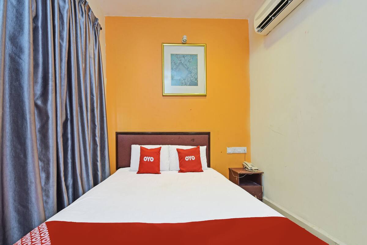 Habitación de hotel con cama, mesita de noche, teléfono y un cuadro en la pared.