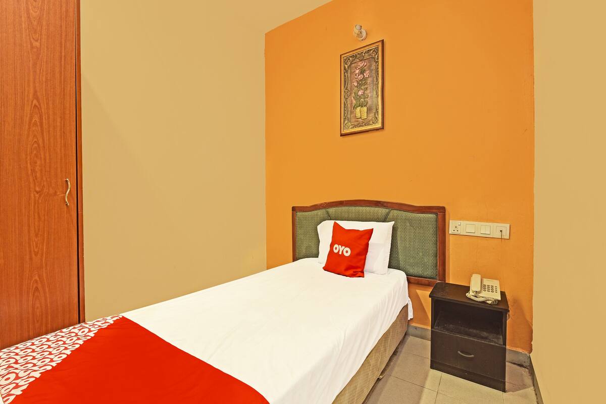 Una habitación de hotel con una cama, una mesita de noche, un teléfono y una lámpara fijada en la pared.