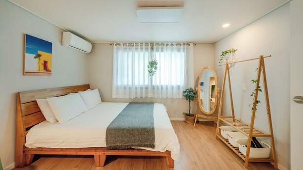 A bedroom with a wooden bed, a bedside mirror, a plant, and a wooden drying rack. - Taean Yoyo Kids Poolvilla (Taean)