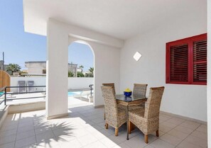 Un balcón con mesa y sillas, una piscina y un persiano rojo.