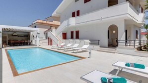 Un hôtel moderne doté d’une piscine, de chaises longues et d’un espace extérieur couvert.