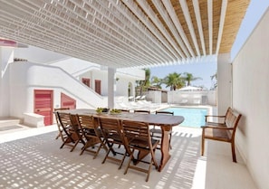Zona junto a la piscina con una mesa y sillas de madera, una piscina y un área de estar techada.