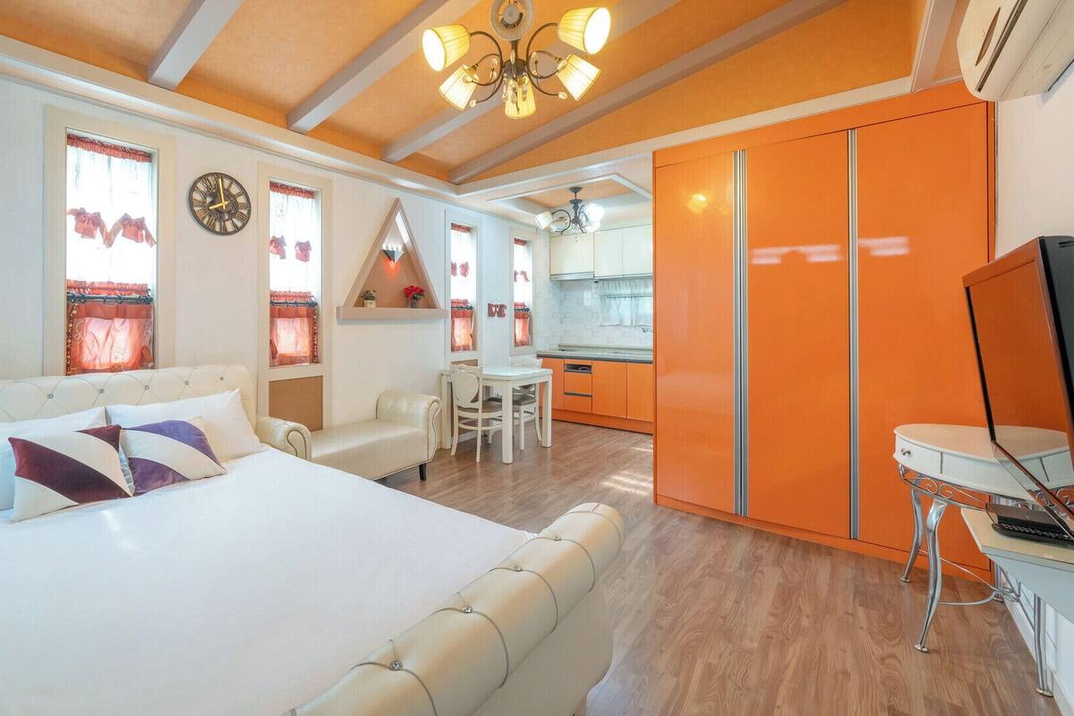 A bedroom with a large bed, a dining area, and a kitchen.