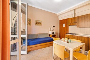 Una cucina compatta con mobili in legno, un tavolo da pranzo con sedie gialle, un divano blu con cuscini a quadretti e un forno a microonde su un tavolino.